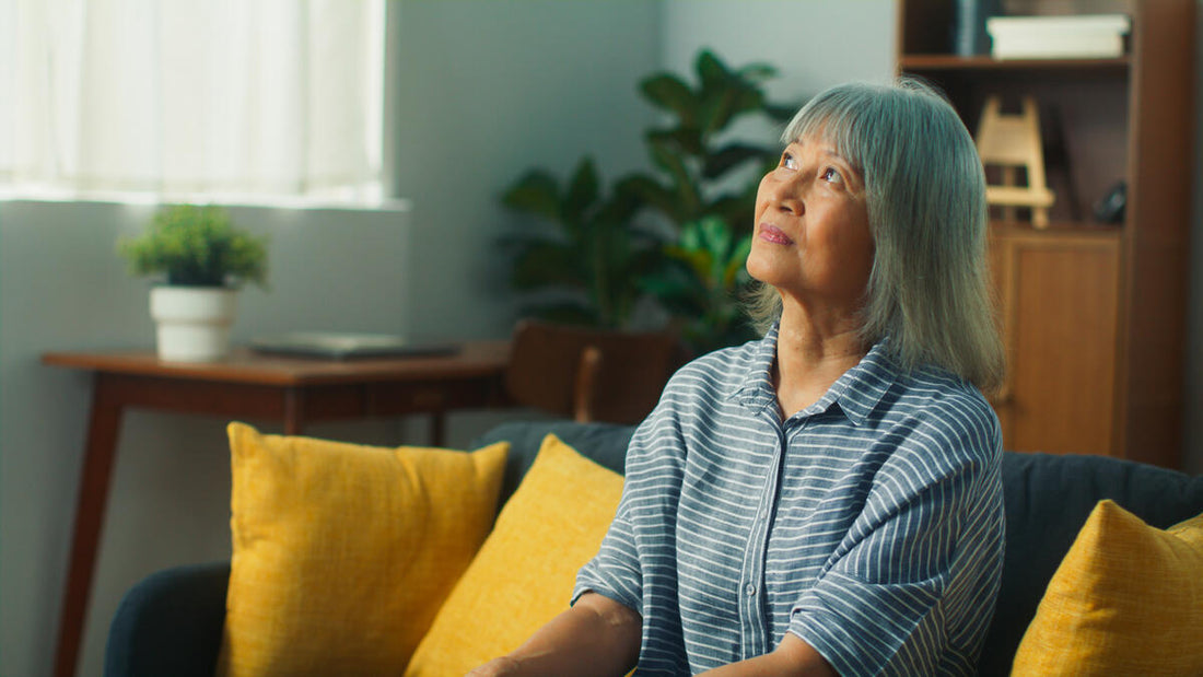 Older woman sitting on a couch at home looking upward thoughtfully in a calm living room