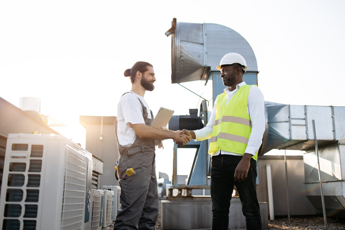 Two HVAC contractors shaking hands on a rooftop next to commercial HVAC equipment