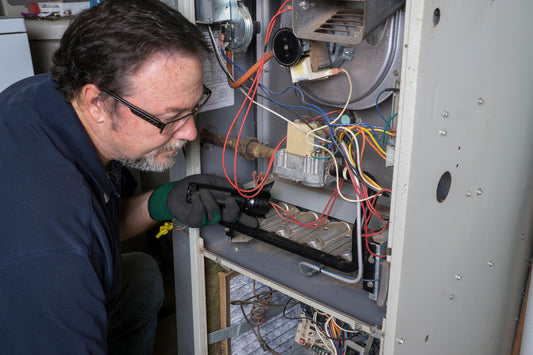 HVAC technician inspecting furnace repair parts inside a gas furnace, including wiring, burners, and internal components during maintenance